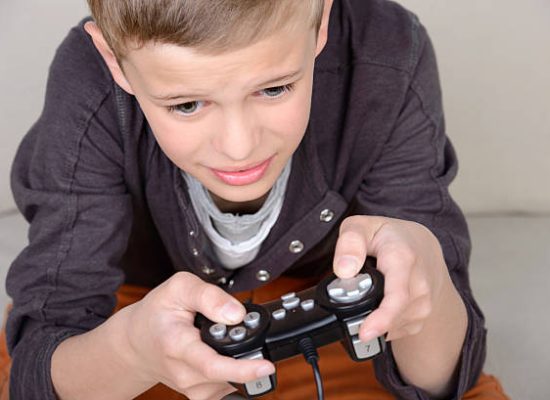 Cute boy playing video games sitting on the sofa at home